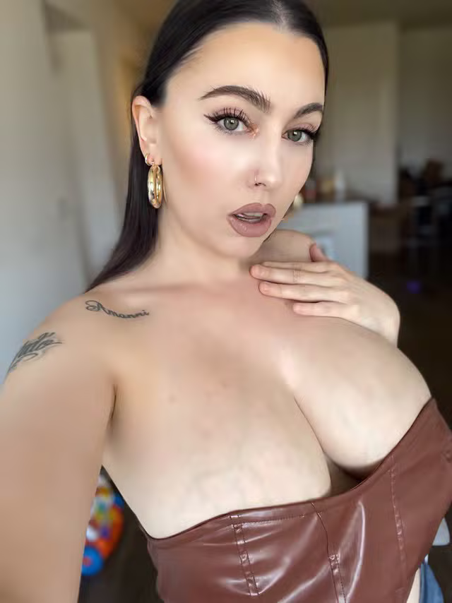 dakotahblue looks alluring in a brown leather corset with sleek dark hair and dramatic makeup.