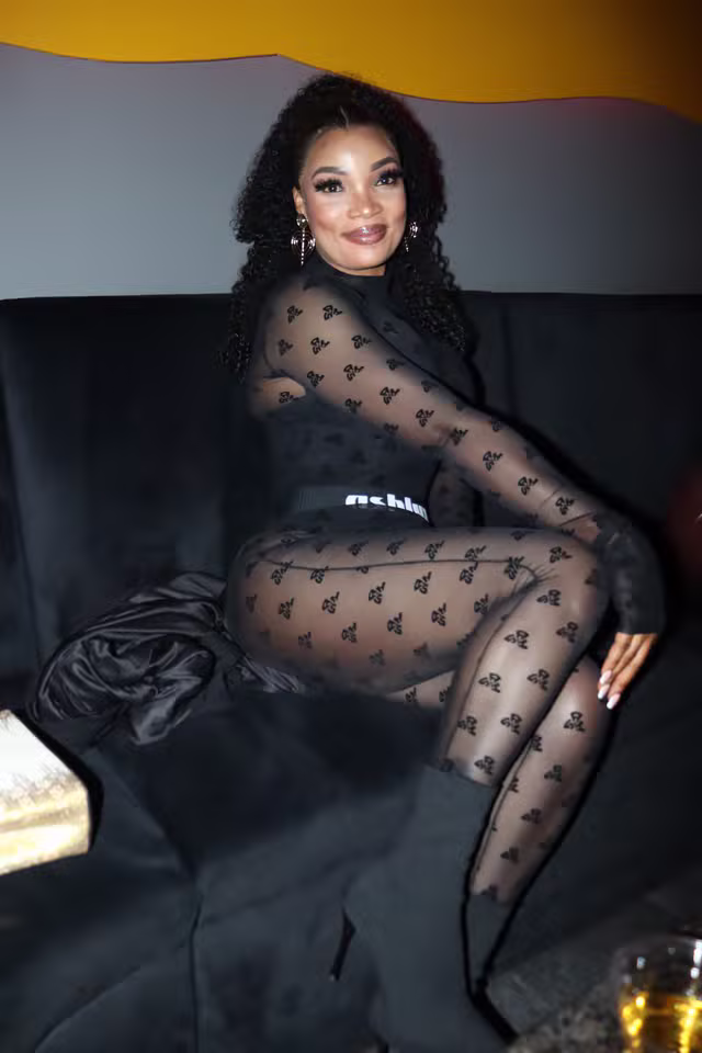 sexy.lexi.gfe smiles confidently in a sheer black butterfly bodysuit with cascading curls.