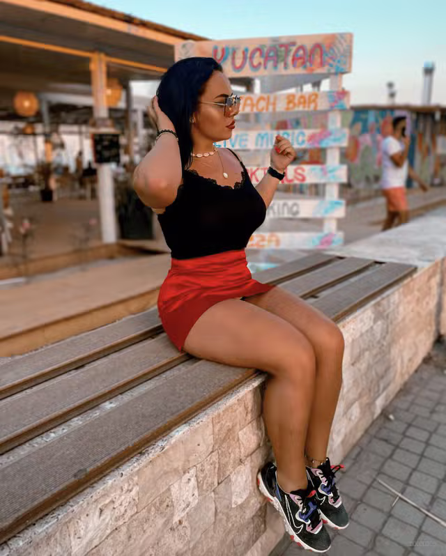 Miss Lila Free sits confidently in a black lace top paired with a red skirt.